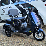 Black electric scooter with a large seat in front of a white van with branding.