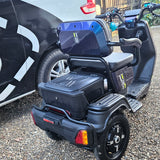 Black mobility scooter on a gravel surface with a car in the background