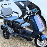 Black mobility scooter with a large seat in front of a white vehicle.