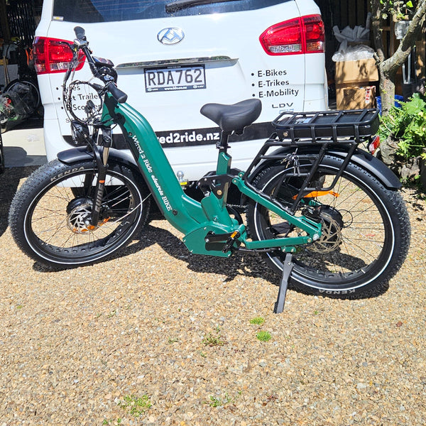 Green electric bike parked on a gravel surface with a white van in the background.