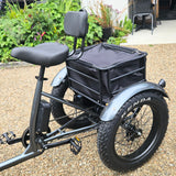 Four-wheeled electric bike with a black basket on a gravel surface with greenery in the background