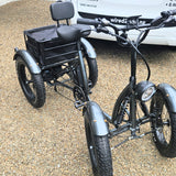 Black four-wheeled electric bike on a gravel surface with a white van in the background.