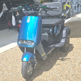 Blue mobility scooter with a visible brand logo on a gravel surface.
