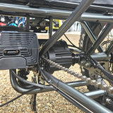 Close-up of a motorcycle chain and sprocket system on a gravel surface.