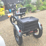 Three-wheeled cargo bike with a black basket in a garden setting