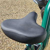 Black bicycle seat on a green bike with gravel background